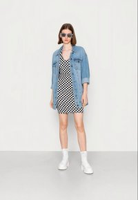 Casaco de ganga sobre um vestido xadrez preto e branco. Bainha curta, combinado com botins brancos com atacadores. Óculos de sol quadrados realçam o visual.