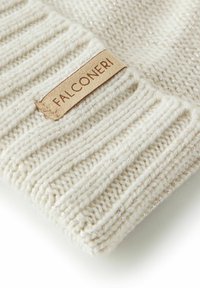 Kremowa dzianinowa czapka z prążkowanym wzorem, subtelnymi metalicznymi nićmi oraz prostokątną miodową skórzaną łatą z napisem "FALCONERI".