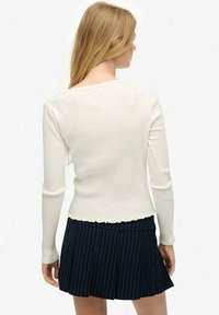 Hvid ribbet langærmet top med en frynset kant, parret med en navy stribet nederdel. Glat tekstur og tætsiddende silhuet.