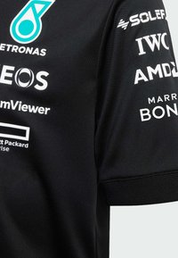 Černý sportovní dres s krátkým rukávem, s bílými sponzorskými logy a modrým akcentovým logem na horním levém rohu. Hladká, lehká tkanina.