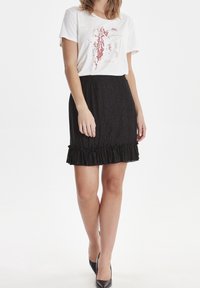 Czarna spódnica w poziome paski z falbaną na dole, w połączeniu z białą koszulką z graficznym wzorem w czerwonych i złotych akcentach.