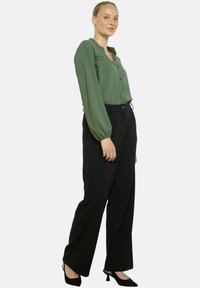 Blusa verde con bottoni e colletto testurizzato, abbinata a pantaloni neri a vita alta e scarpe col tacco nere. Tessuti morbidi e vestibilità ampia.