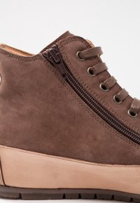 Bottine compensée en daim marron avec fermeture éclair latérale et lacets marron assortis, avec œillets en métal et semelle en caoutchouc.