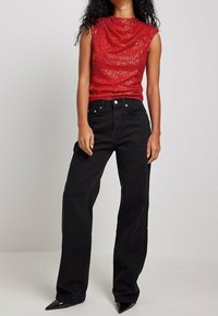 Haut sans manches rouge à paillettes avec décolleté drapé associé à un jean droit noir taille haute et des escarpins noirs à bout pointu.
