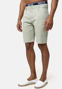 Hellgrüne Shorts mit strukturiertem Muster, ausgestattet mit einem Knopfverschluss und Gürtelschlaufen. Kombiniert mit weißen Espadrilles.