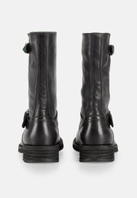 Botas de tobillo de cuero negro con un diseño ajustado. Presentan una textura arrugada, una pequeña correa lateral y un tacón apilado.