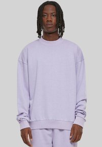 Sweatshirt oversized en lavande avec des manches longues, col et poignets côtelés, en matière polaire douce, surface légèrement texturée, coupe décontractée.