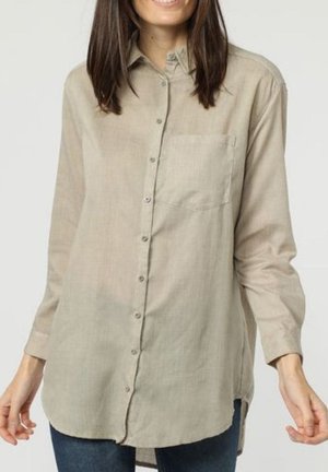 Camisa de manga larga con botones en tejido beige claro, que cuenta con un bolsillo en el pecho, dobladillo redondeado y un ajuste relajado. Material suave y texturizado.