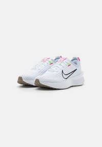 Bílé sportovní boty s prodyšným vrškem, černým logem swoosh, růžovými a zelenými akcenty a šedou gumovou podrážkou. Zaoblený design paty.