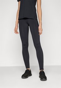 Juodos sportinės legging kelnės, pagamintos iš elastingos medžiagos, su lygiu paviršiumi ir prigludusia forma, derinamos su juodais sportiniais batais.