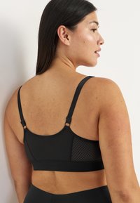Zwarte sportbeha met mesh panelen. Verstelbare bandjes en haak-en-oogsluiting. Gladde textuur, minimalistisch ontwerp en ondersteunende structuur.