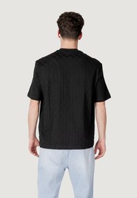 Camisetta nera a maniche corte con un motivo a diamante testurizzato. Vestibilità rilassata, taglio dritto e colletto rotondo. Indossata con pantaloni azzurri chiari.