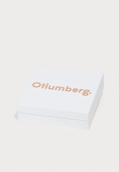 Hvid rektangulær kasse med en glat overflade, der har præget tekst "Otiumberg." i lysebrune bogstaver på toppen.