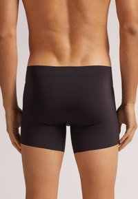 Černé, elastické boxerky s hladkým povrchem, s nízkým pasem a krátkou délkou nohavic, navržené pro pohodlí a správné padnutí.