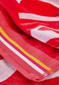 Asciugamano da spiaggia rosso con motivi astratti bianchi e rosa, bordi a righe in rosa, giallo e bianco; tessuto testurizzato.