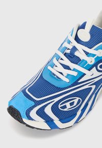 Blue athletic shoe with mesh and synthetic materials, featuring white accents, a textured sole, and distinctive wave-like patterns.