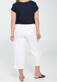 Námořnický top s ohrnutými rukávy v kombinaci s bílými zkrácenými kalhotami, které mají uvolněný střih a hladkou texturu. Na nohou jednoduché hnědé sandály.