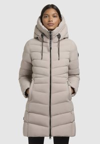 Manteau matelassé beige clair avec un col haut, un design en chevrons, une fermeture éclair à l'avant, des cordons de serrage ajustables et des poches latérales.