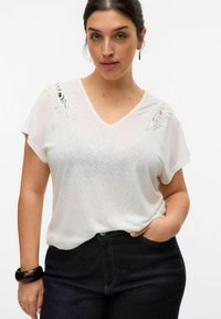 White short-sleeve V-neck top with lace detailing on the shoulders. Soft fabric and relaxed fit. Paired with dark denim jeans.