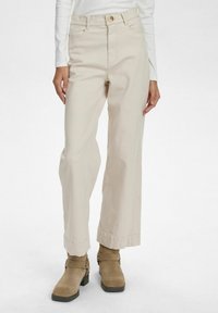 Beiga vida byxor i bomull med hög midja, bälteshällor och frams pockets. Matchas med bruna ankelstövlar.