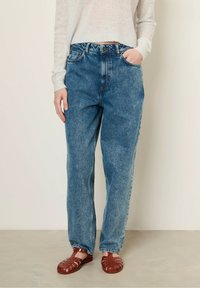 Verbleekte blauwe denim rechtlopende jeans met een hoge taille, vijf zakken en een knoopsluiting, gecombineerd met rode gevlochten sandalen.