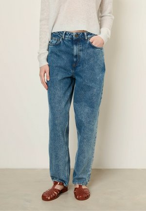 Verbleekte blauwe denim rechtlopende jeans met een hoge taille, vijf zakken en een knoopsluiting, gecombineerd met rode gevlochten sandalen.