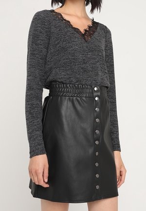 Jupe mini en cuir noir avec une taille haute à texture froncée et une fermeture à bouton à l'avant. Haut gris à manches longues avec un col en dentelle.