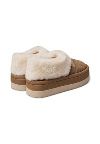 Pantofole con zoccolo marrone, dotate di una morbida fodera in pelliccia sintetica color crema, forma arrotondata e suola testurizzata. Presentano un'accademia cucita sul lato.