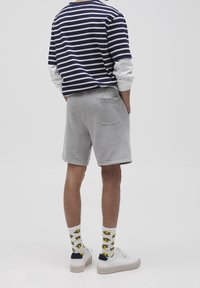 Chemise à rayures bleu marine et blanche à manches longues sur un short gris, avec des chaussettes blanches à motifs jaunes et des baskets blanches.