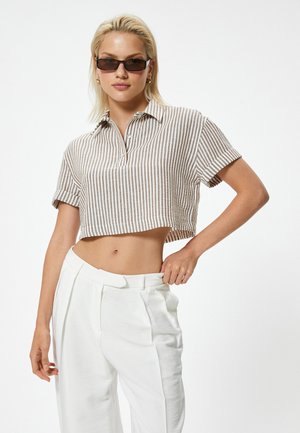 Camisa a rayas recortada en lino beige y blanco con cuello y tapeta de botones, combinada con pantalones blancos de tiro alto.