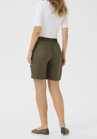 Szorty w kolorze oliwkowej zieleni z elastycznym pasem, do kolan o gładkiej fakturze, zestawione z dopasowanym białym topem i brązowymi balerinami.