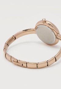 Ρολόι βραχιόλι από μεταλλικό ροζ χρυσό με συνδεδεμένο λουράκι, στρογγυλή πίσω θήκη και μικρό κρύσταλλο στην κορώνα, επώνυμο Swarovski.