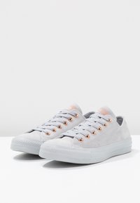 Sneaker grigio in suede con occhielli color oro rosa, punta tonda, suola piatta in gomma e lacci grigi chiari. Accentazioni testurizzate sulla linguetta e sul lato.