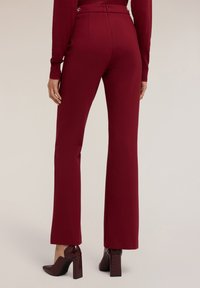 Bordeaux-kleurige op maat gemaakte broek met een vlakke voorkant, taps toelopende pijpen en ritssluiting, gecombineerd met glanzende bordeaux-kleurige block-heeled schoenen.
