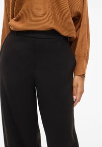 Brun ribbet genser og høyt verdsatte svarte vide bukser, med glatt stoff og subtile sideslitser. Minimalistisk design med strømlinjeformede linjer.