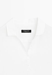 Biała koszulka polo z kołnierzykiem, trzema guzikami oraz czarną metką z napisem „Massimo Dutti Made in China” wewnątrz kołnierza.