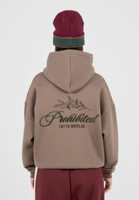 Sweat à capuche marron avec un grand logo comportant le mot "Interdit" et "10119 BERLIN" en noir, conçu avec une coupe décontractée et une capuche.