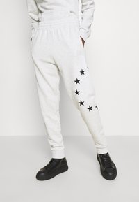 Grå mjukisbyxor med elastisk midja, dekorerade med svarta stjärntryck längs ena benet. Kombinerade med svarta sneakers med tjock sula.