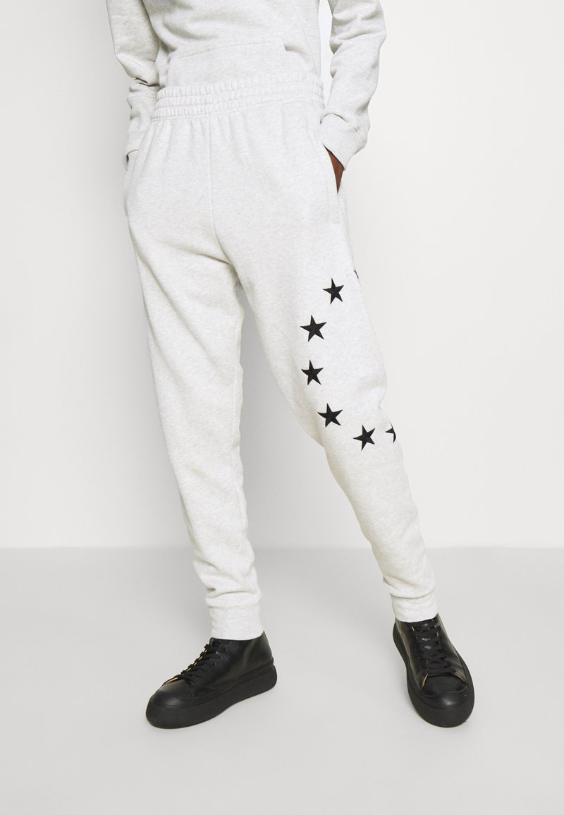 Grå mjukisbyxor med elastisk midja, dekorerade med svarta stjärntryck längs ena benet. Kombinerade med svarta sneakers med tjock sula.