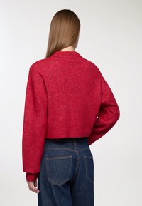 Maglione rosso corto in un morbido knit, con un ampio colletto e spalle basse, abbinato a jeans in denim scuro a vita alta.