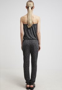 Jumpsuit a strisce nere e grigie con design off-the-shoulder, gambe affusolate e una texture di tessuto morbido. Indossato con calzature scure.