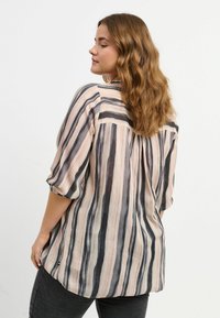 Blusa a righe in tessuto morbido con linee orizzontali nere, rosa e crema. Maniche corte e vestibilità rilassata con orlo arrotondato.
