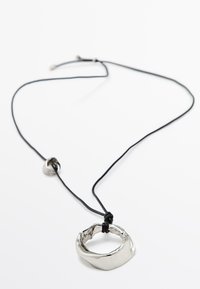 Pendentif en argent de forme irrégulière et organique, suspendu à un cordon noir avec une perle métallique ronde. Texture de surface lisse et brillante.