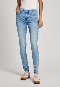 Ljusblå skinny jeans med fem fickor, dragkedja och knappstängning, som matchas med blekrosa sneakers med marinblå detaljer.