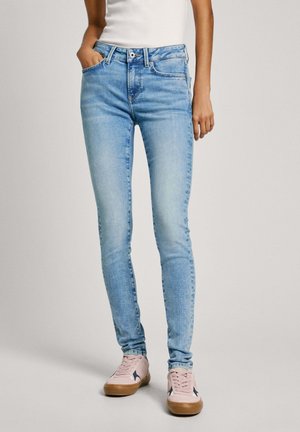 Hellblaue Skinny-Jeans mit fünf Taschen, Reißverschluss und Knopfverschluss, kombiniert mit hellroten Sneakers mit marinefarbenen Akzenten.