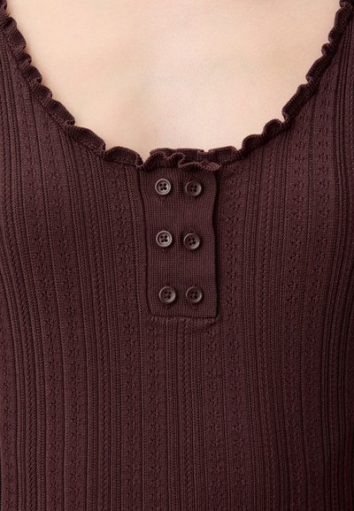 Top marrone in maglia a coste con scollo smerlato, caratterizzato da quattro bottoni marroni su una pattina testurizzata.