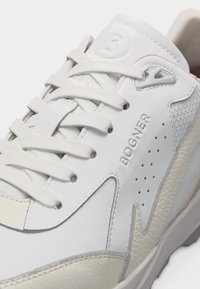 Baskets en cuir blanc avec accents beige, lacets blancs, panneau latéral perforé et logo "BOGNER" embossé sur le côté.
