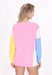 Svetr s barevnými bloky ve fialových, žlutých, bílých a modrých prvcích. Měkká tkanina, dlouhé rukávy a volný střih.