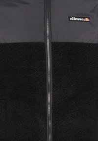 Černá bunda s prošívanou horní částí a texturovanou fleecovou spodní částí, středovým zipem a logem na hrudi.