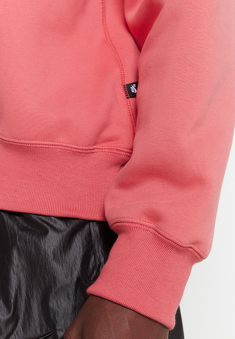 Korallowy sweatshirt z prążkowanymi mankietami i dekoltem, wykonany z miękkiej tkaniny. Zawiera czarną metkę z logo na bocznym szwie.